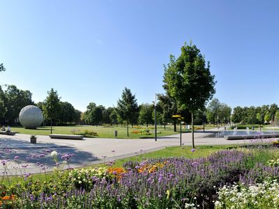Das Bild zeigt einen Park im Sommer mit schön angelegten Wegen und blühenden Blumen in Beeten.